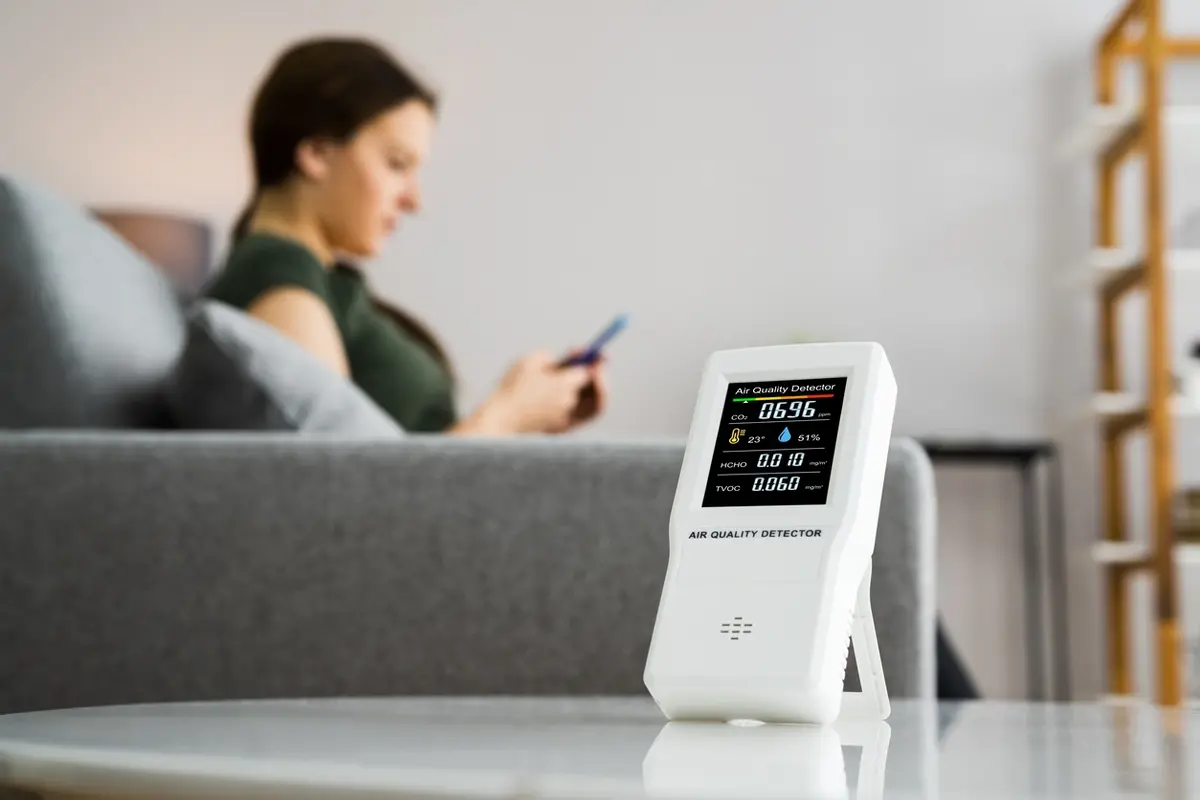 Homeowner relaxing on her couch next to an indoor air quality monitor